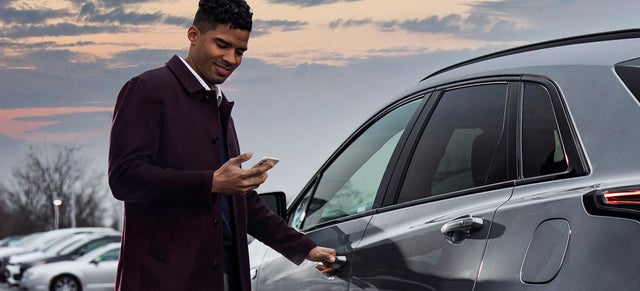 A man looking at his cell phone prepares to enter a vehicle