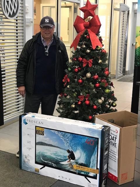 A man in the North Bay Cadillac dealership standing next to a boxed flat-screen TV and a Christmas Tree