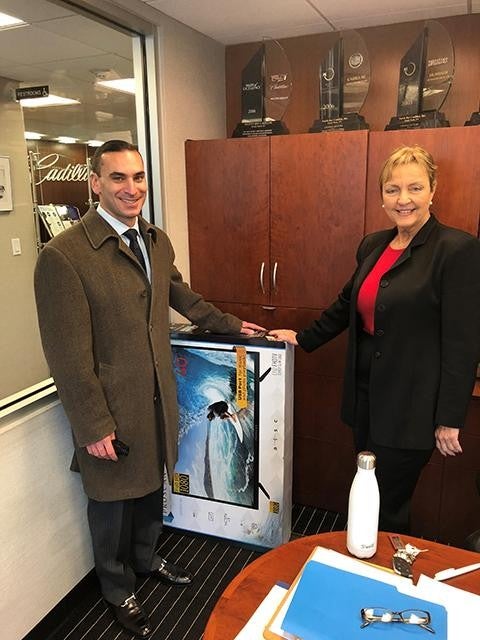 A woman and man in an office at North Bay Cadillac standing next to a boxed flat-screen TV