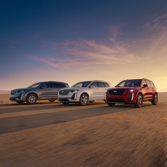 Three Quarters View of Silver, White and Red Cadillac XT6s Parked with a Sunset Behind Them