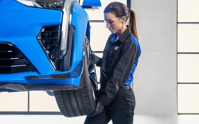 A Certified Cadillac Service Technician removing a front wheel from a raised vehicle