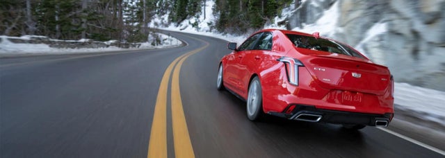 A Cadillac CT4 AWD driving down a road in a forested winter landscape